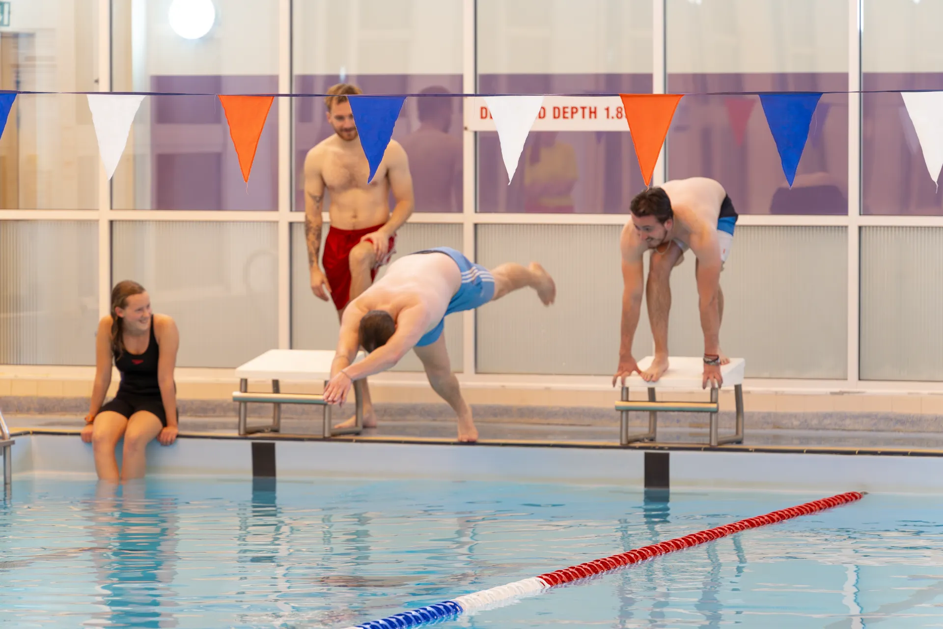 Man diving into the swimming pool while being watched by his friends